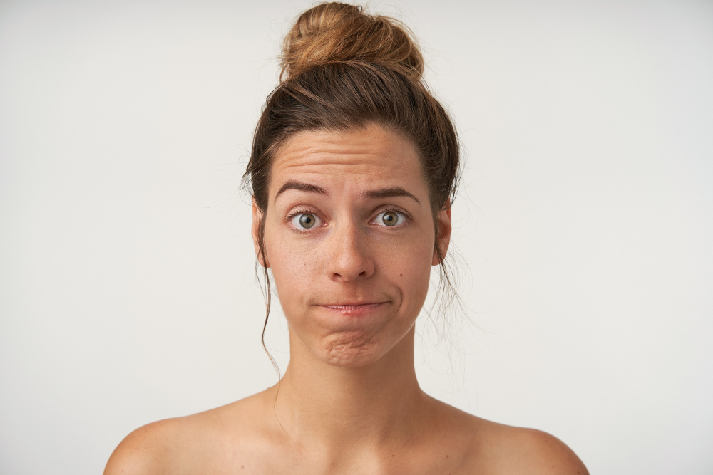 portrait-young-pretty-woman-looking-with-raised-eyebrow-twisted-lips-wearing-high-bun-hairstyle-no-make-up-being-disappointed